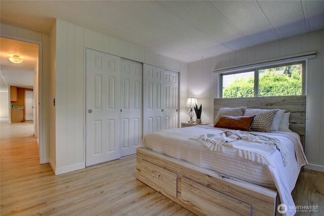 bedroom featuring wood walls, a closet, baseboards, and light wood-style floors