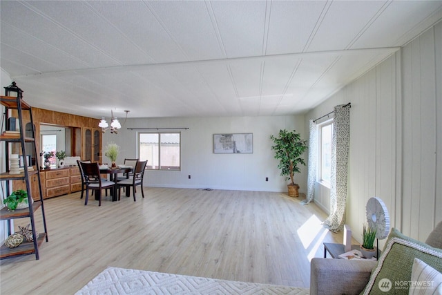 living room with a chandelier, wood walls, and light wood-style floors
