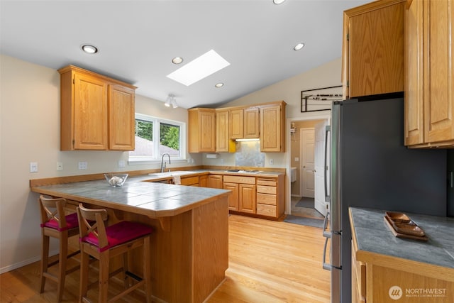 kitchen featuring a skylight, a peninsula, a sink, gas cooktop, and freestanding refrigerator
