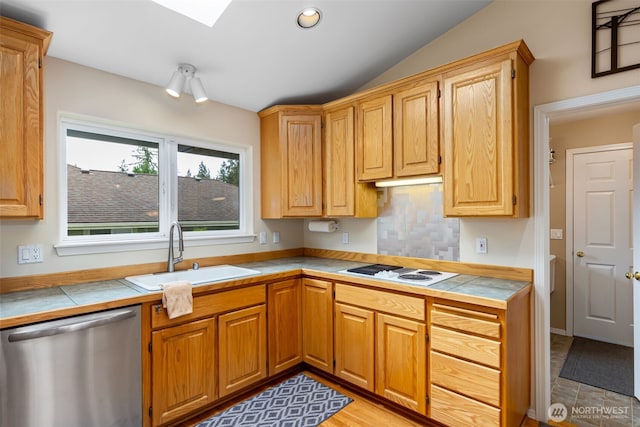 kitchen with stainless steel dishwasher, a sink, tile counters, white electric cooktop, and lofted ceiling