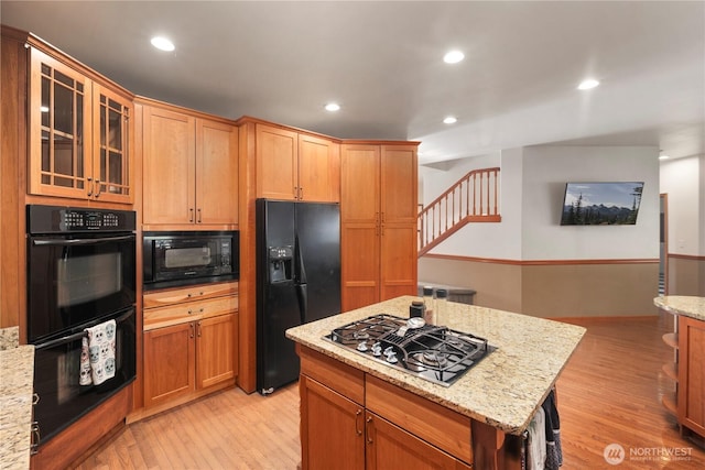 kitchen featuring black appliances, light wood-type flooring, light stone countertops, glass insert cabinets, and recessed lighting