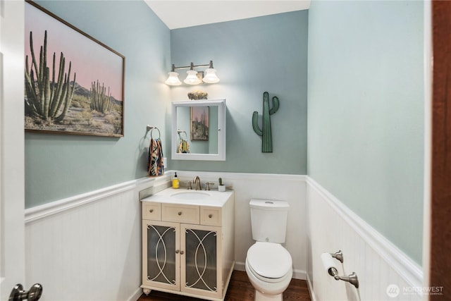 half bath with wainscoting, toilet, vanity, and wood finished floors