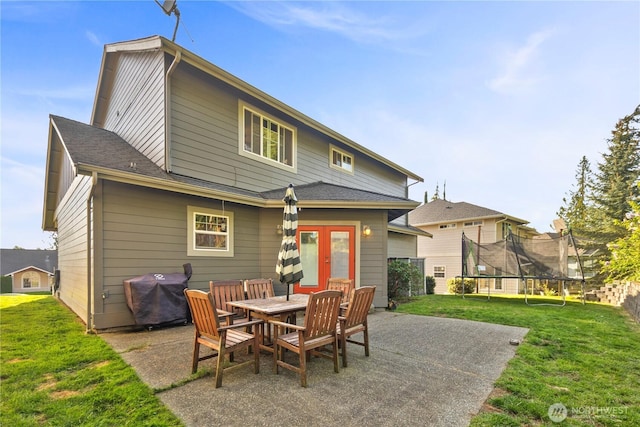 rear view of house featuring a patio area, a trampoline, a lawn, french doors, and outdoor dining space