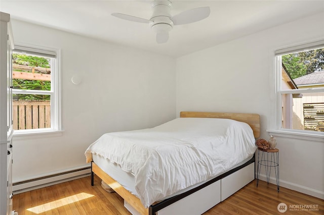 bedroom with wood finished floors, a ceiling fan, baseboard heating, and multiple windows