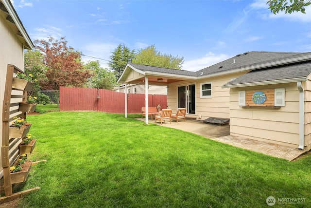 rear view of property featuring a yard, a patio area, a shingled roof, and fence