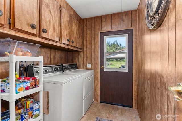 clothes washing area featuring separate washer and dryer, wooden walls, and cabinet space