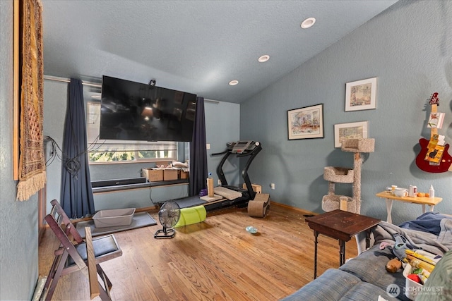 workout area featuring vaulted ceiling, wood finished floors, baseboards, and a textured ceiling
