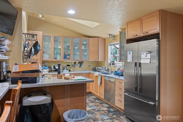 kitchen with stainless steel appliances, a skylight, vaulted ceiling, glass insert cabinets, and light brown cabinets