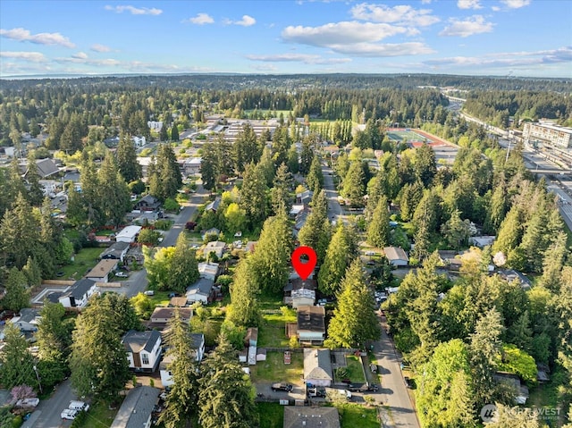 aerial view of property and surrounding area featuring a forest and nearby suburban area