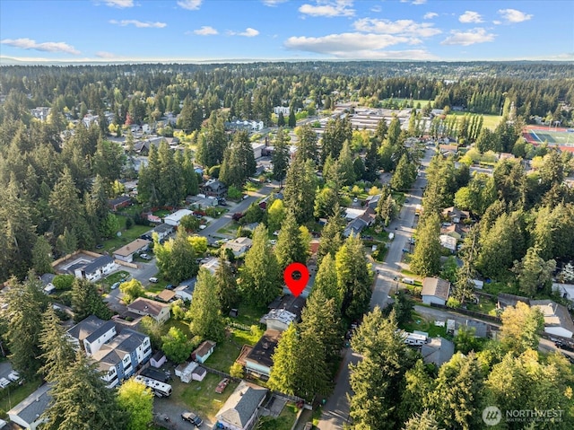 aerial view of property and surrounding area featuring nearby suburban area and a heavily wooded area