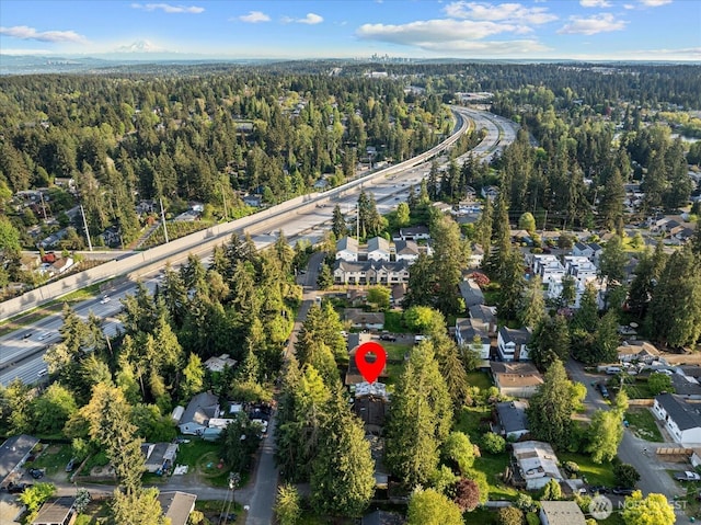 aerial view of property and surrounding area featuring a forest and nearby suburban area