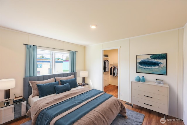 bedroom with a walk in closet, ornamental molding, a closet, and wood finished floors