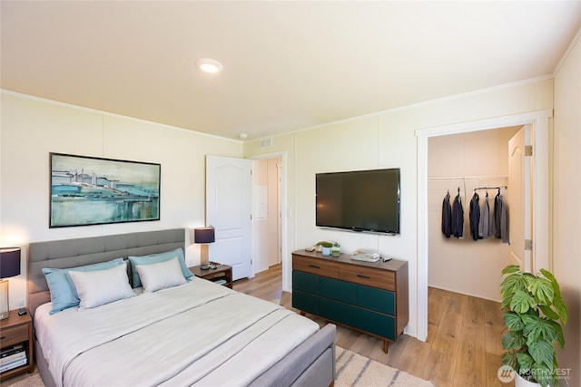 bedroom featuring a closet, ornamental molding, visible vents, a walk in closet, and light wood-style floors