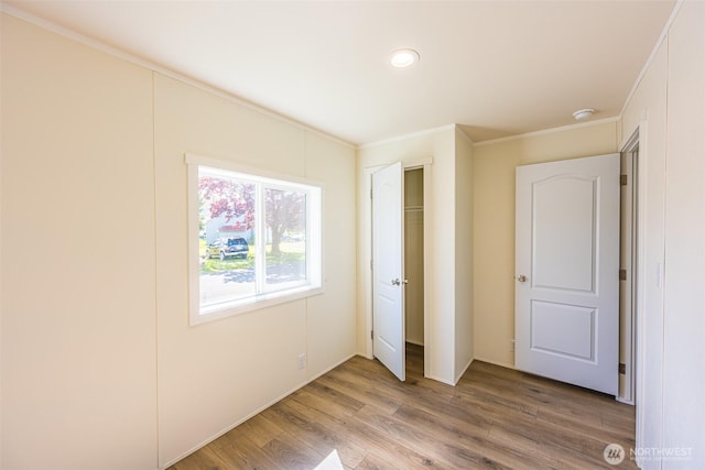 unfurnished bedroom with recessed lighting, a closet, crown molding, and wood finished floors