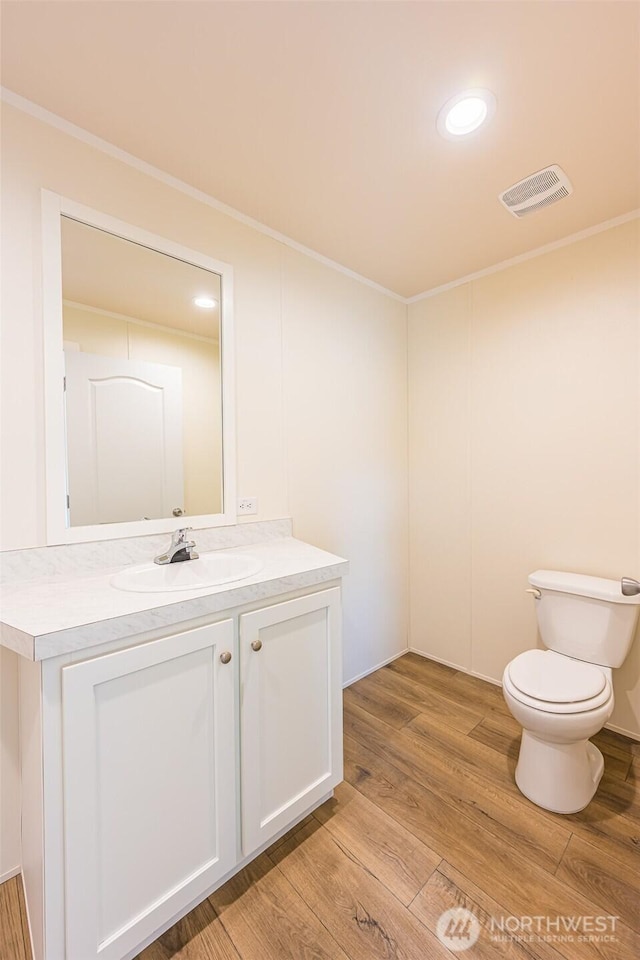 half bathroom featuring toilet, wood finished floors, vanity, ornamental molding, and visible vents