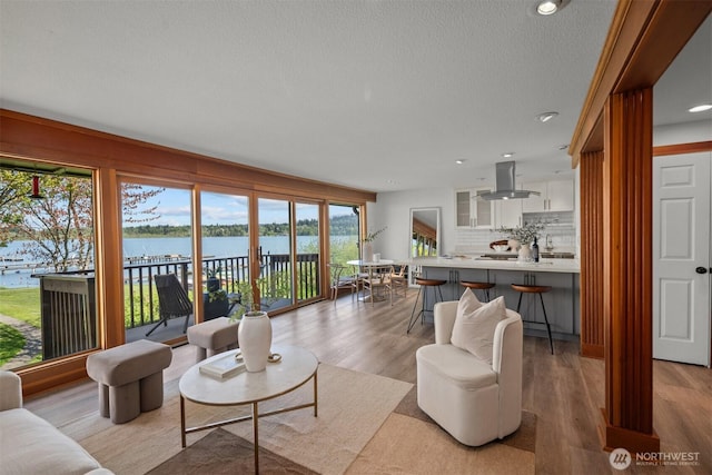living area featuring a textured ceiling, healthy amount of natural light, light wood finished floors, a water view, and recessed lighting
