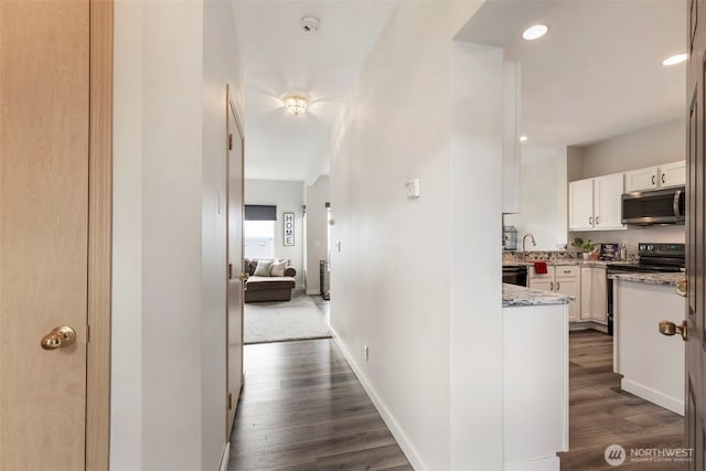 hallway with dark wood finished floors, baseboards, and recessed lighting
