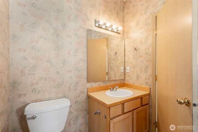 half bath with wallpapered walls, toilet, and vanity