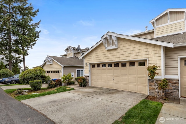 view of front facade featuring stone siding, a garage, driveway, and roof with shingles