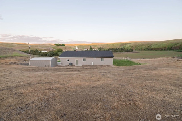 back of property with a lawn, a rural view, an outdoor structure, and a storage unit