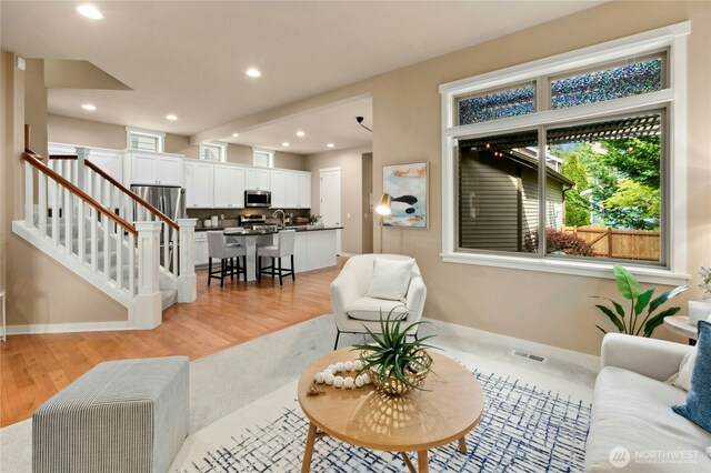 living room with plenty of natural light, stairway, light wood-style flooring, baseboards, and recessed lighting