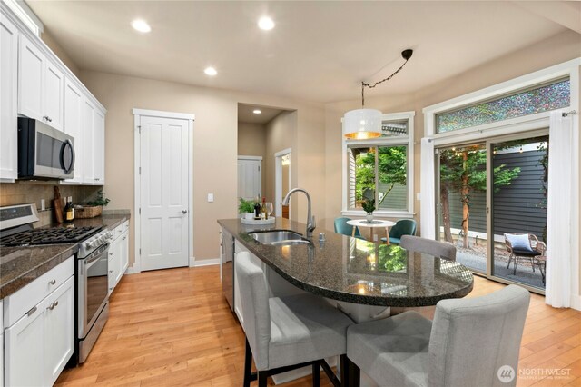 kitchen with stainless steel appliances, a sink, a kitchen breakfast bar, decorative backsplash, and light wood finished floors