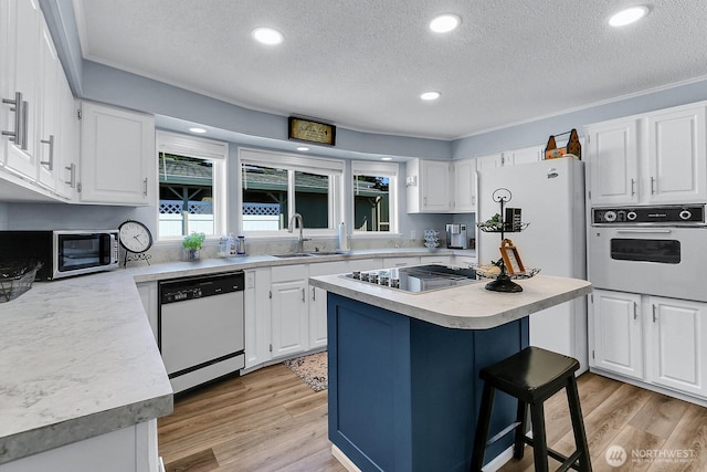 kitchen with a textured ceiling, white appliances, white cabinetry, and a sink