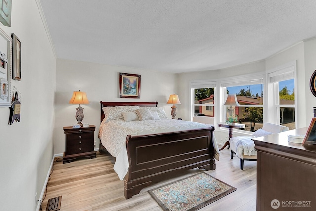 bedroom featuring light wood-style floors, visible vents, baseboards, and a textured ceiling