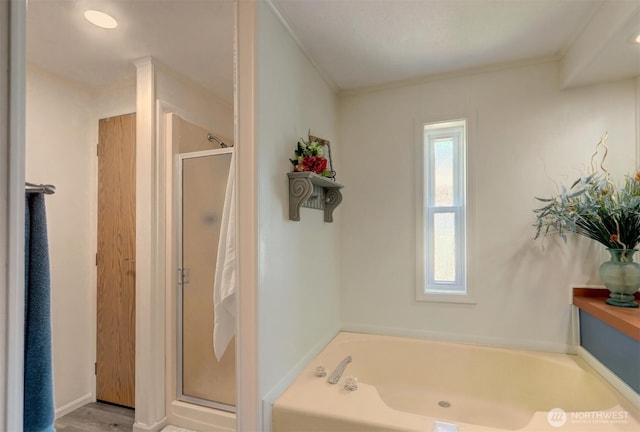 bathroom featuring a stall shower, ornamental molding, a garden tub, and wood finished floors