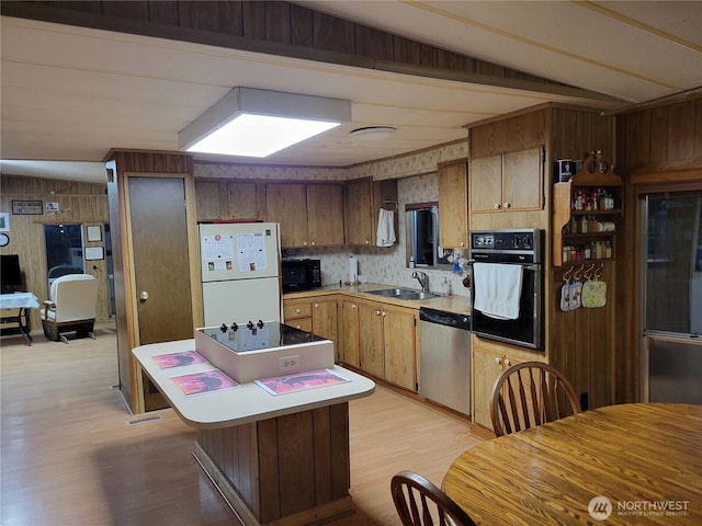 kitchen featuring a sink, wood walls, light wood-type flooring, black appliances, and a center island