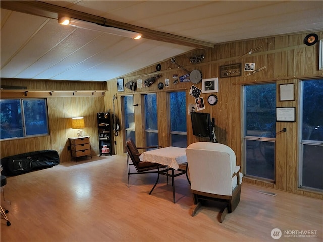 dining room with wooden walls, lofted ceiling with beams, and wood finished floors