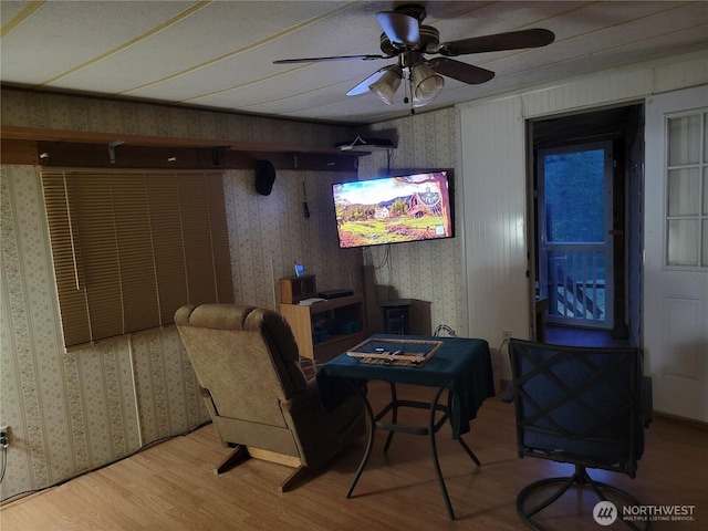 living area featuring a ceiling fan, wallpapered walls, and wood finished floors