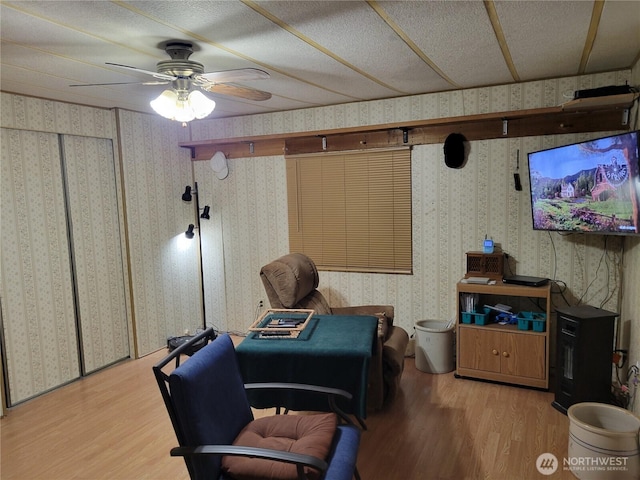 living area with wood finished floors, wallpapered walls, and ceiling fan