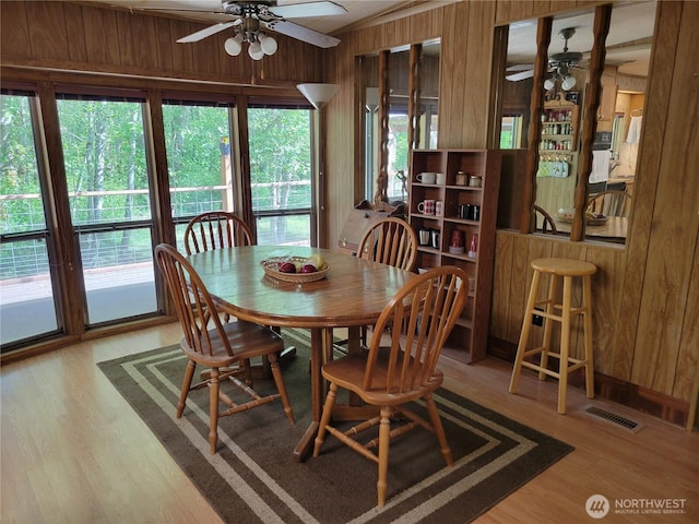 dining room featuring ceiling fan, wooden walls, and wood finished floors