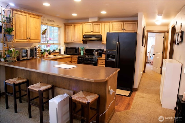 kitchen with black appliances, under cabinet range hood, a peninsula, light carpet, and a breakfast bar area