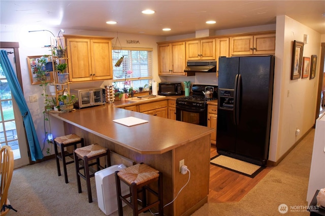 kitchen with black appliances, under cabinet range hood, a sink, a peninsula, and a kitchen breakfast bar