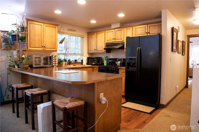 kitchen featuring black appliances, under cabinet range hood, a peninsula, a kitchen bar, and recessed lighting