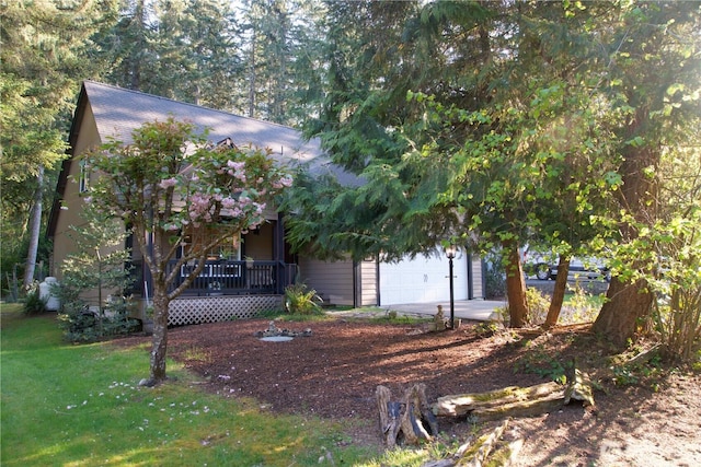 view of property hidden behind natural elements with a front yard, a garage, covered porch, and a shingled roof
