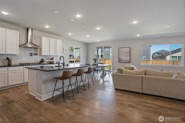 kitchen with wall chimney exhaust hood, open floor plan, dark countertops, stainless steel gas cooktop, and recessed lighting