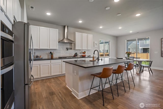 kitchen with wall chimney exhaust hood, dark countertops, appliances with stainless steel finishes, dark wood finished floors, and recessed lighting