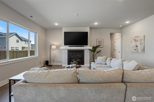 living room with dark wood-style floors, baseboards, recessed lighting, and a glass covered fireplace