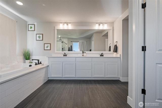 bathroom with a bath, a stall shower, wood finished floors, and double vanity