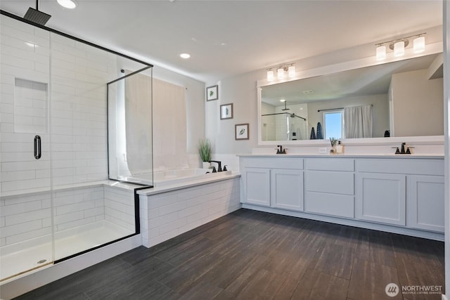 bathroom with a shower stall, a garden tub, double vanity, wood finished floors, and recessed lighting