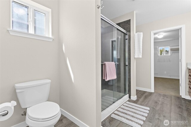 bathroom with a shower stall, wood finished floors, toilet, baseboards, and a walk in closet