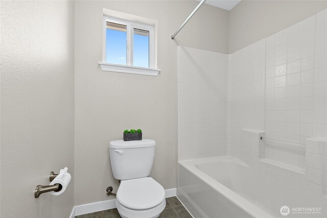 bathroom with baseboards, toilet, and  shower combination