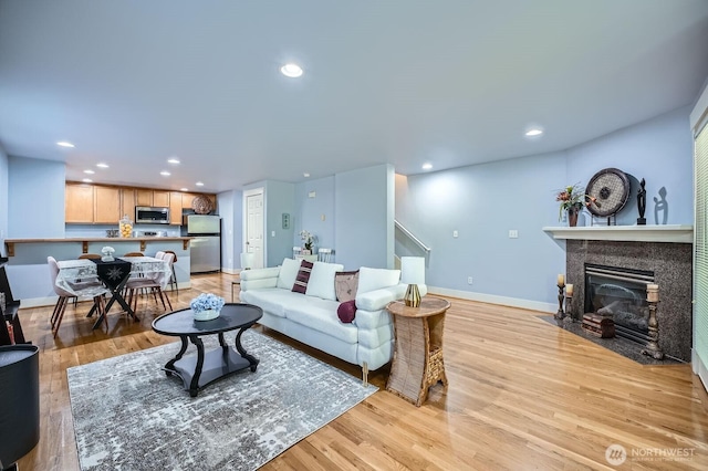 living area featuring light wood-style floors, a fireplace with flush hearth, baseboards, and recessed lighting