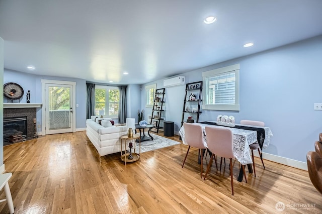 living area featuring an AC wall unit, wood finished floors, a glass covered fireplace, recessed lighting, and baseboards