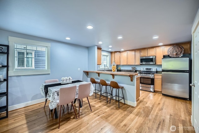 kitchen with stainless steel appliances, light wood finished floors, a peninsula, a breakfast bar, and a sink