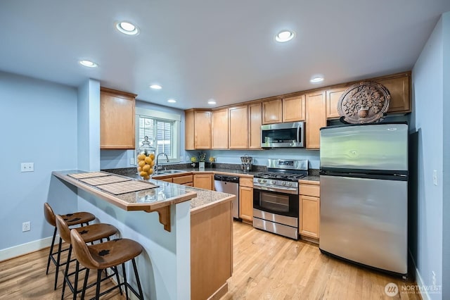kitchen featuring stainless steel appliances, a sink, a kitchen bar, light brown cabinetry, and light wood-style floors