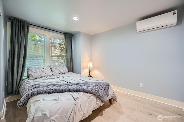 bedroom with a wall unit AC, wood finished floors, baseboards, and recessed lighting